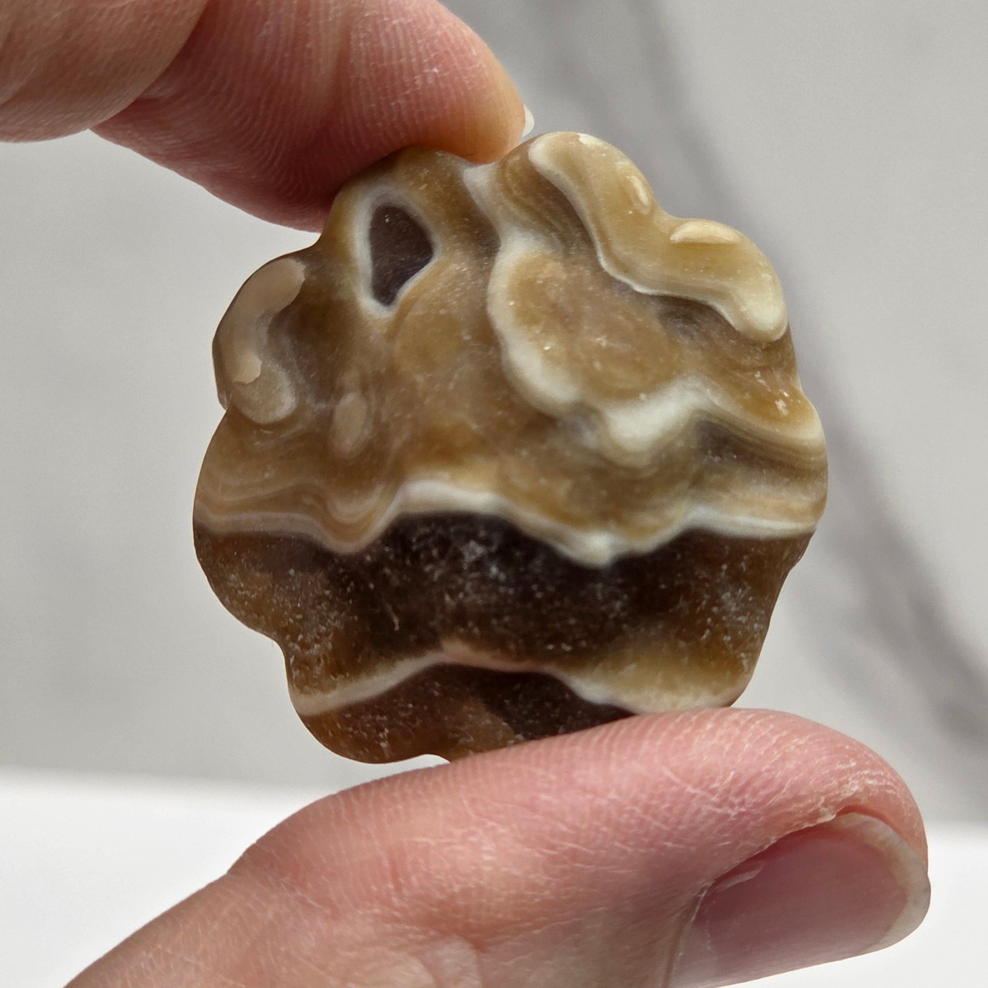 Hand holding an amber calcite sunflower carving against a white background