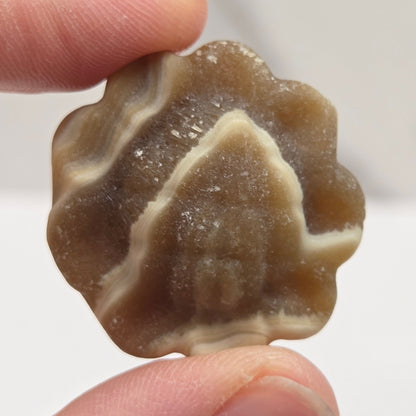 Hand holding an amber calcite  sunflower carving against a white background