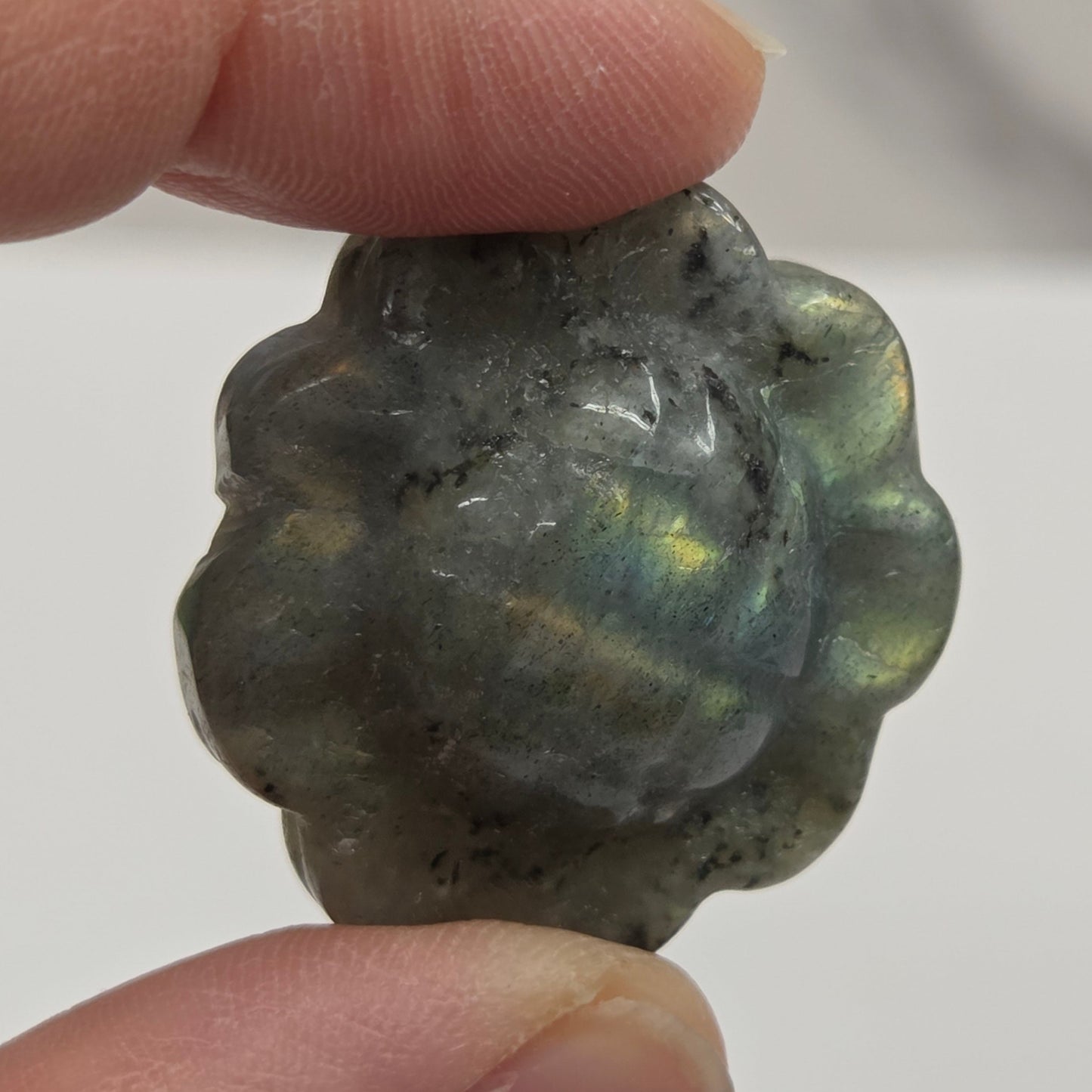 Hand holding a labradorite sunflower carving against a white background