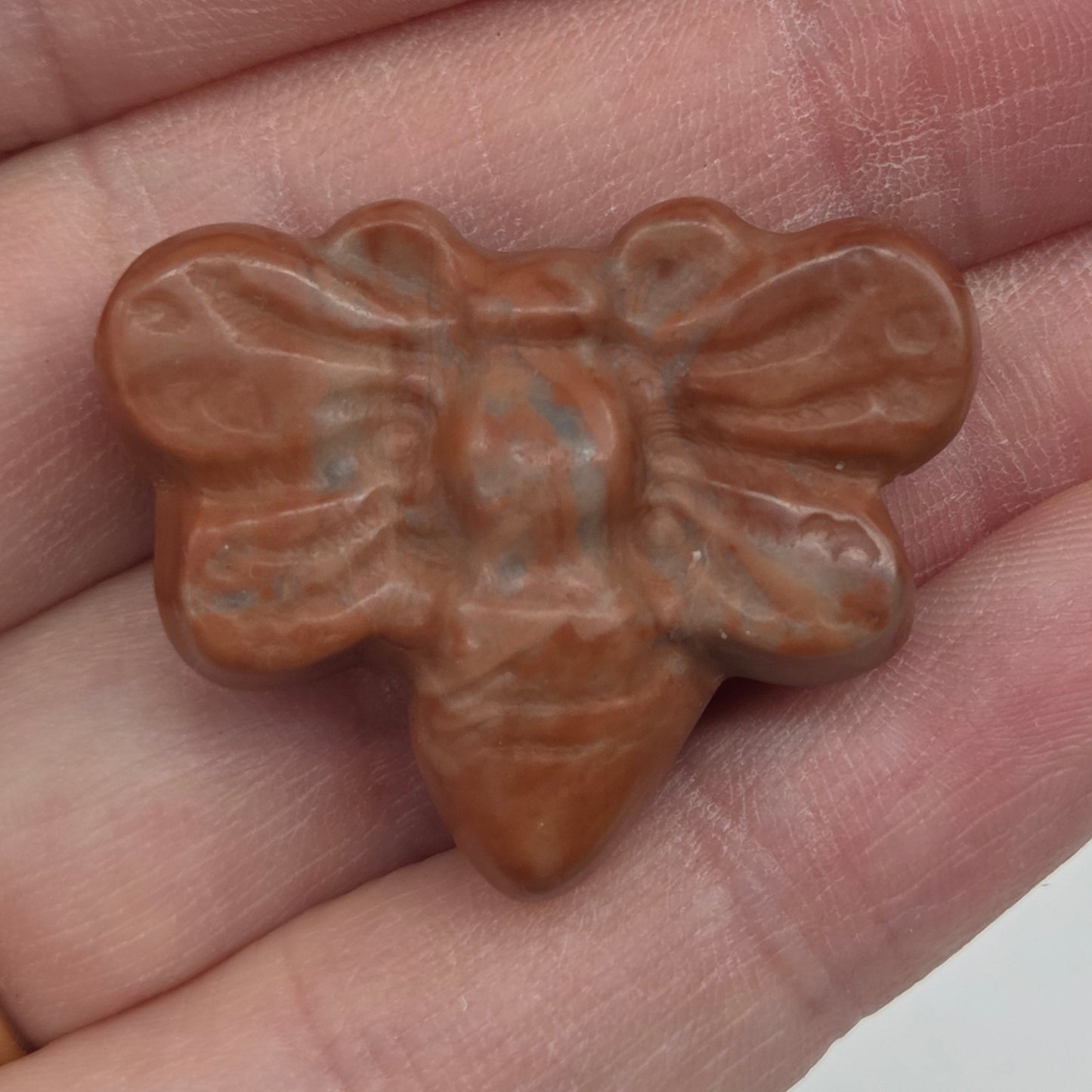 Red Jasper butterfly carving held in a hand against a white background