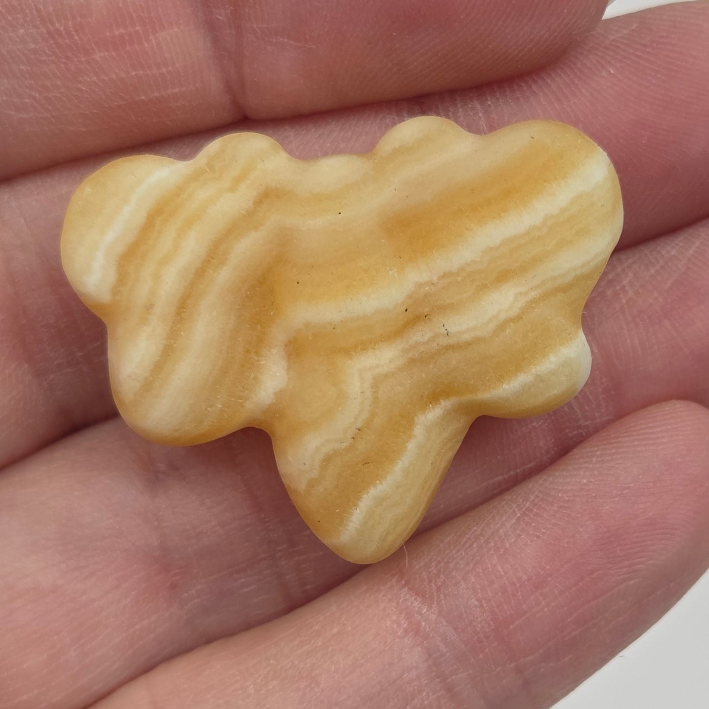 Orange Calcite butterfly carving held in a hand against a white background