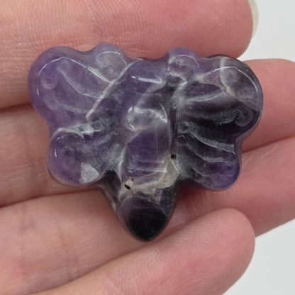 Dream Amethyst butterfly carving held in a hand against a white background