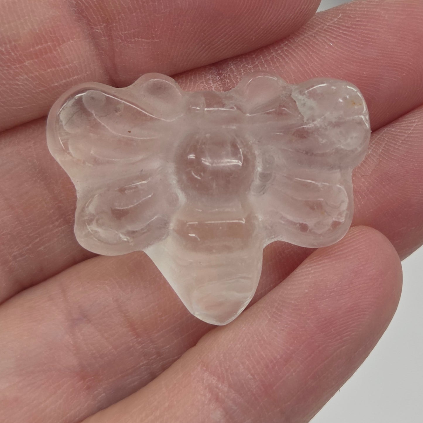 Clear Quartz butterfly carving held in a hand against a white background