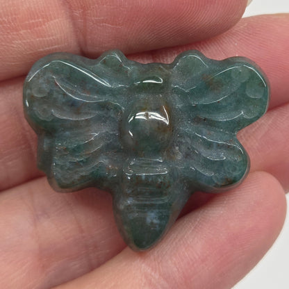 Moss Agate butterfly carving held in a hand against a white background
