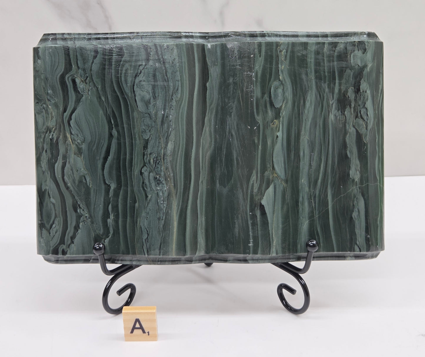 Green wave picture jasper carving made to resemble an open book, on a stand, on a white background. Book has wave-like patterns.