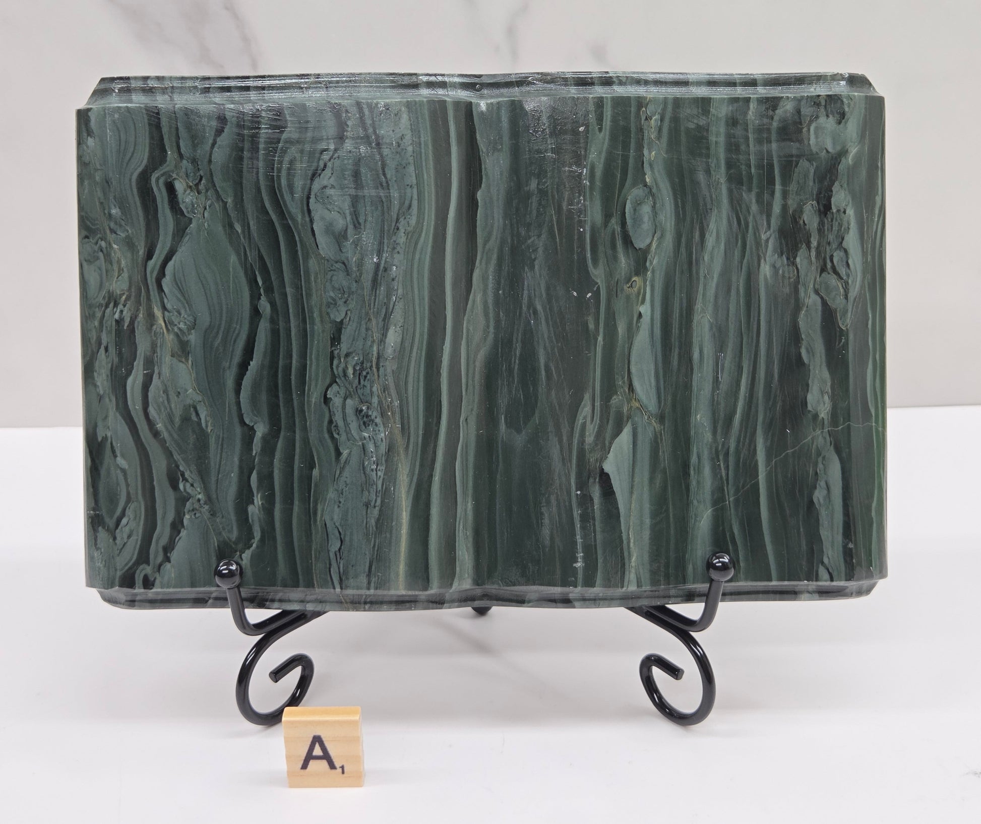 Green wave picture jasper carving made to resemble an open book, on a stand, on a white background. Book has wave-like patterns.