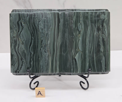 Green wave picture jasper carving made to resemble an open book, on a stand, on a white background. Book has wave-like patterns.