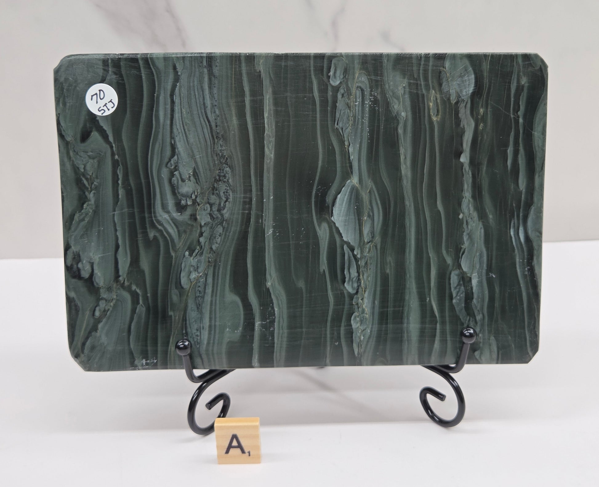 Green wave picture jasper carving made to resemble an open book, on a stand, on a white background. Book has wave-like patterns.