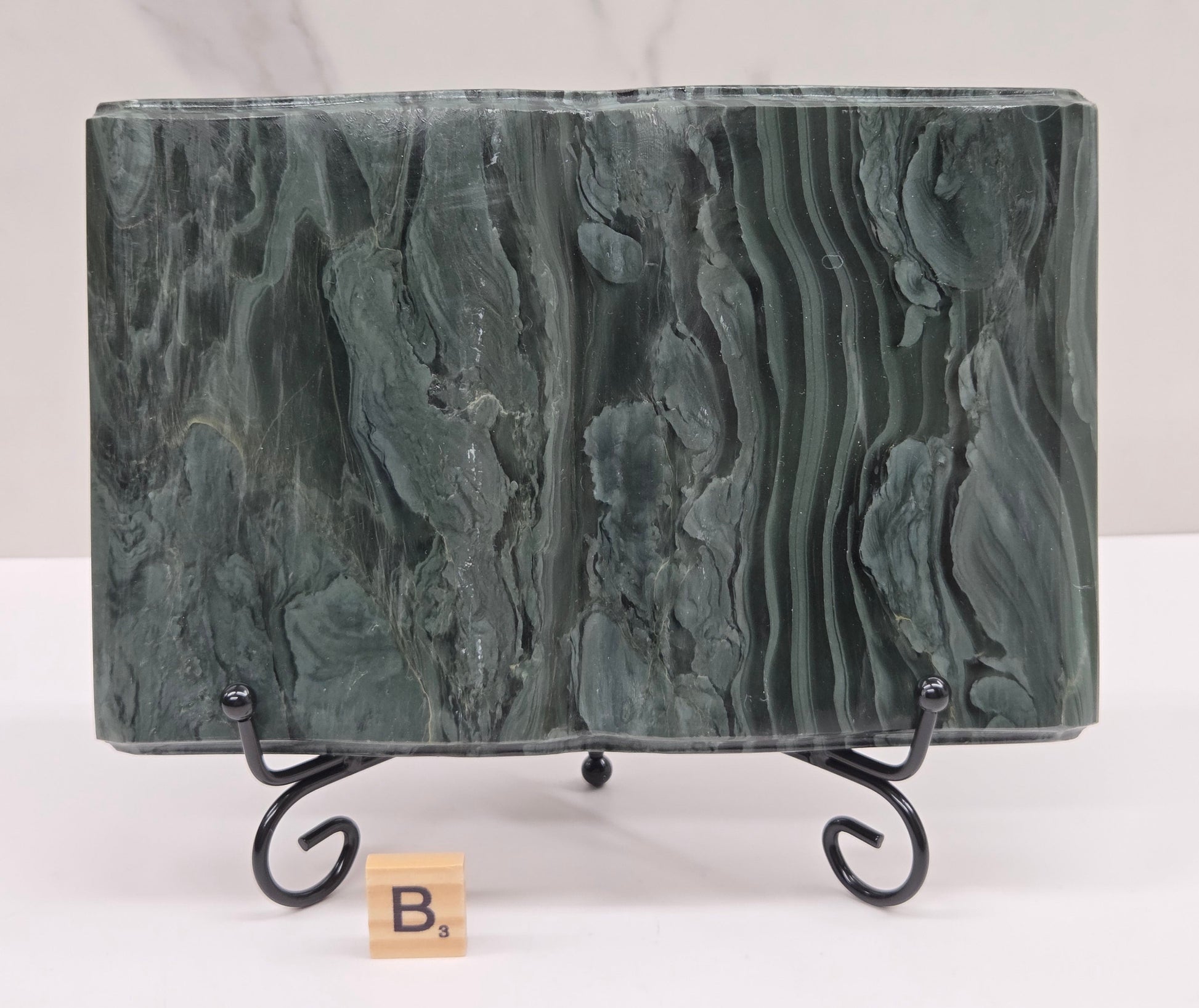 Green wave picture jasper carving made to resemble an open book, on a stand, on a white background. Book has wave-like patterns.