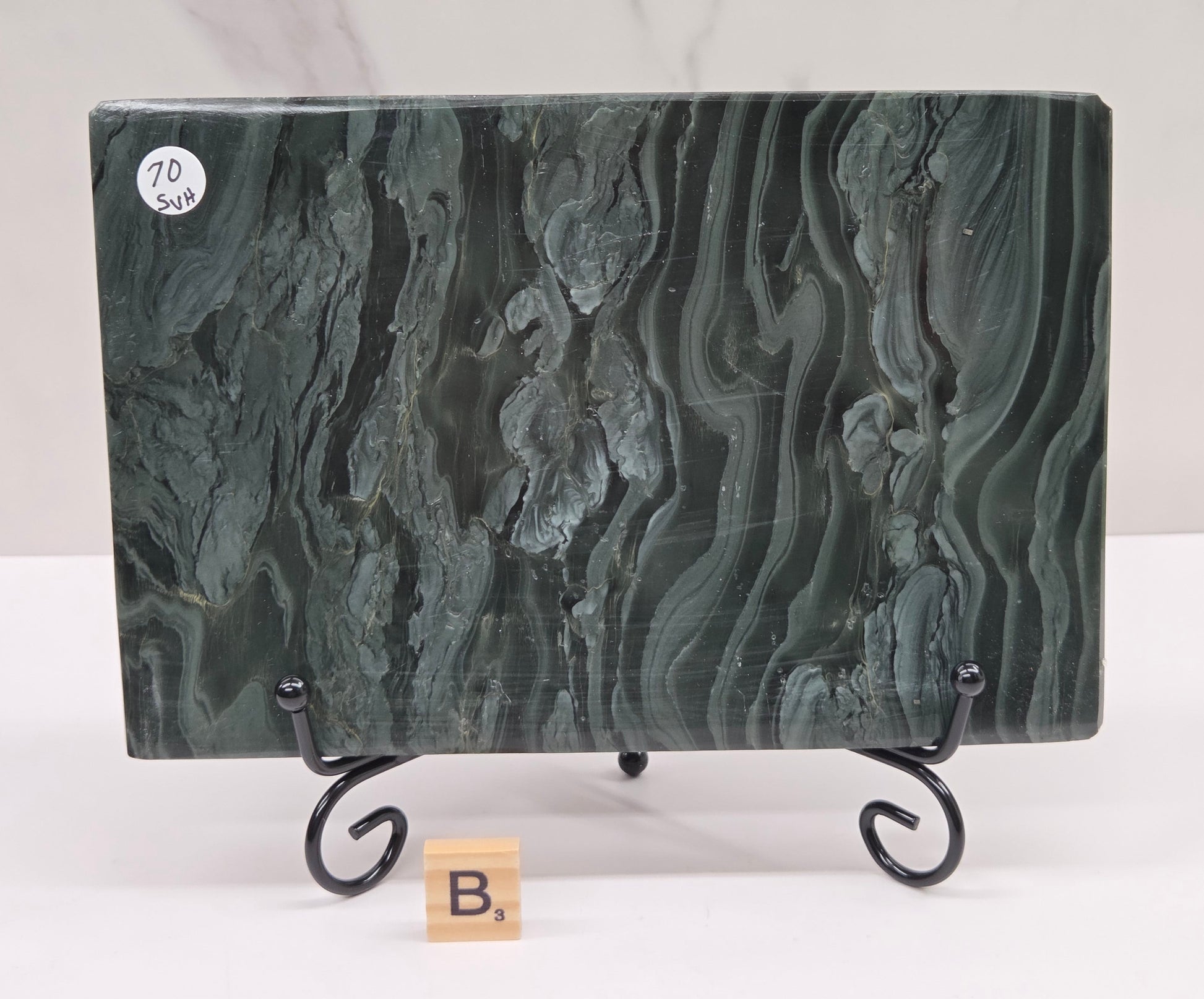 Green wave picture jasper carving made to resemble an open book, on a stand, on a white background. Book has wave-like patterns.