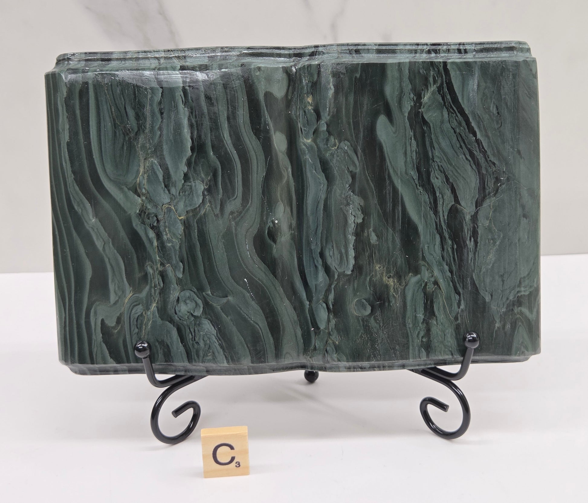 Green wave picture jasper carving made to resemble an open book, on a stand, on a white background. Book has wave-like patterns.