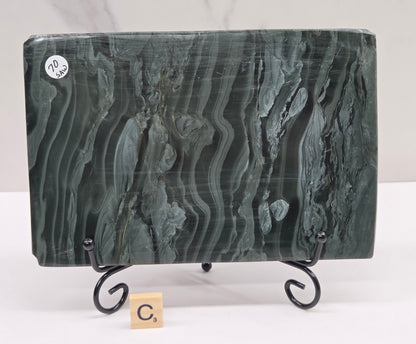 Green wave picture jasper carving made to resemble an open book, on a stand, on a white background. Book has wave-like patterns.