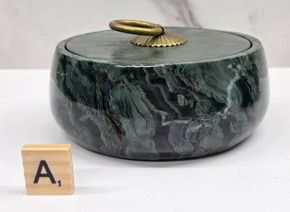 Round bowl container, with a gold colored handle on the lid, made of green wave picture jasper, with wave like patterns, on a white background