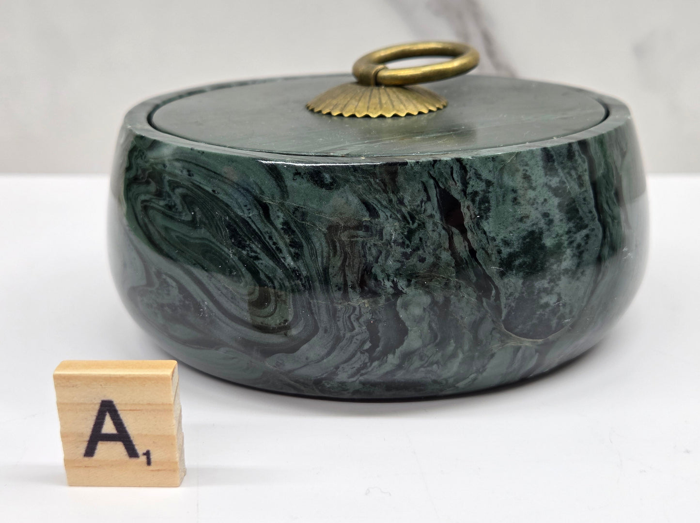 Round bowl container, with a gold colored handle on the lid, made of green wave picture jasper, with wave like patterns, on a white background