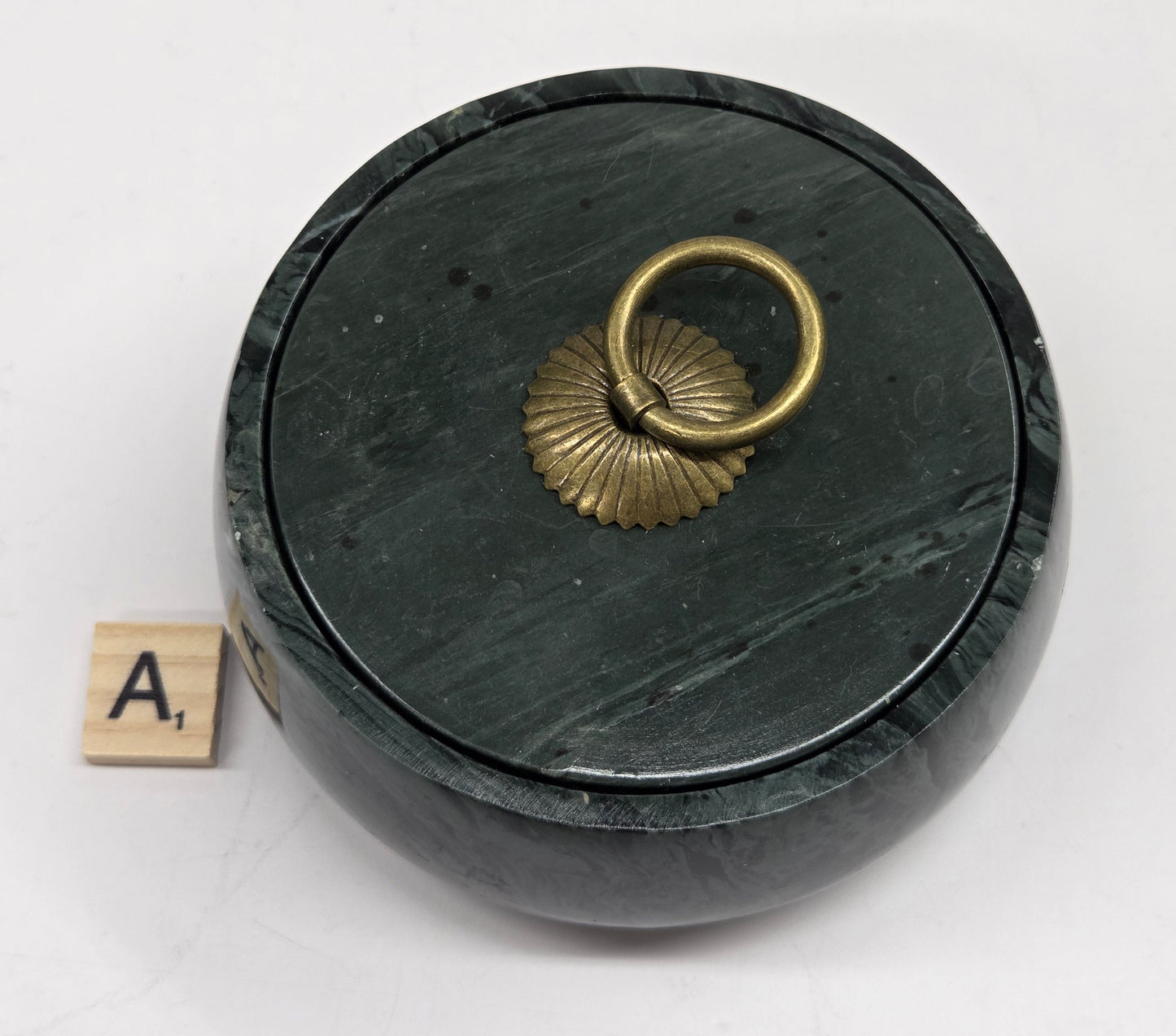 Round bowl container, with a gold colored handle on the lid, made of green wave picture jasper, with wave like patterns, on a white background