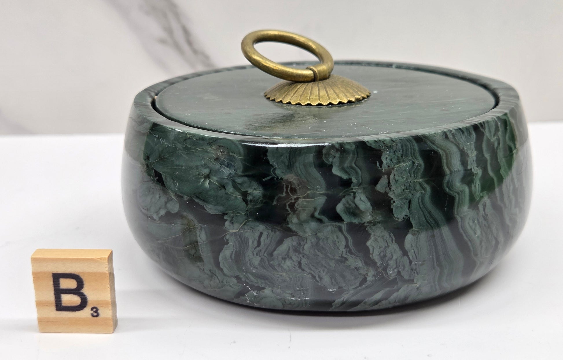 Round bowl container, with a gold colored handle on the lid, made of green wave picture jasper, with wave like patterns, on a white background
