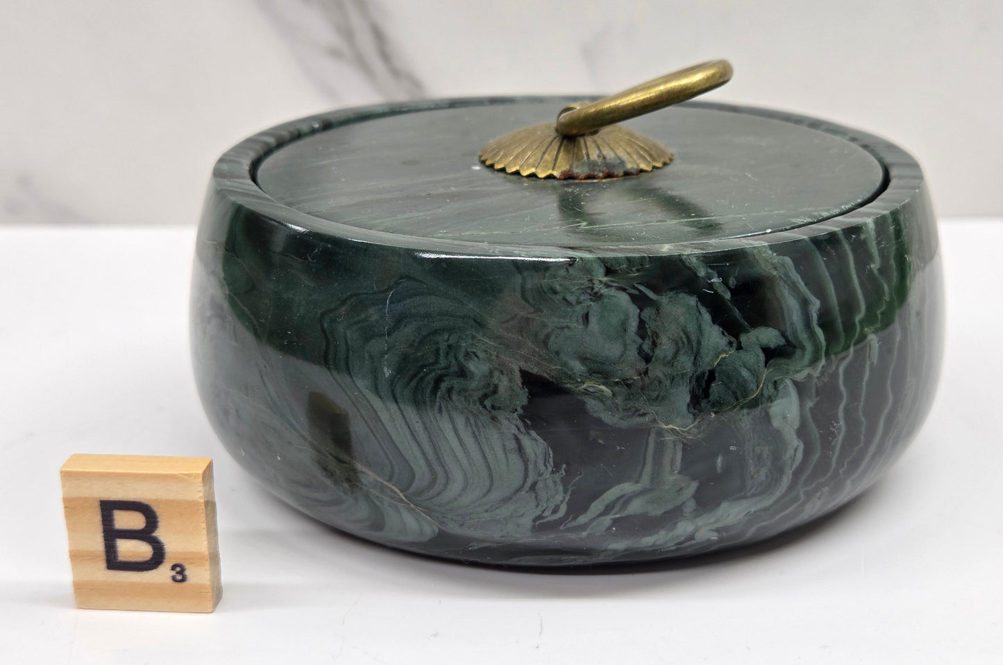 Round bowl container, with a gold colored handle on the lid, made of green wave picture jasper, with wave like patterns, on a white background