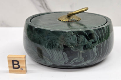 Round bowl container, with a gold colored handle on the lid, made of green wave picture jasper, with wave like patterns, on a white background