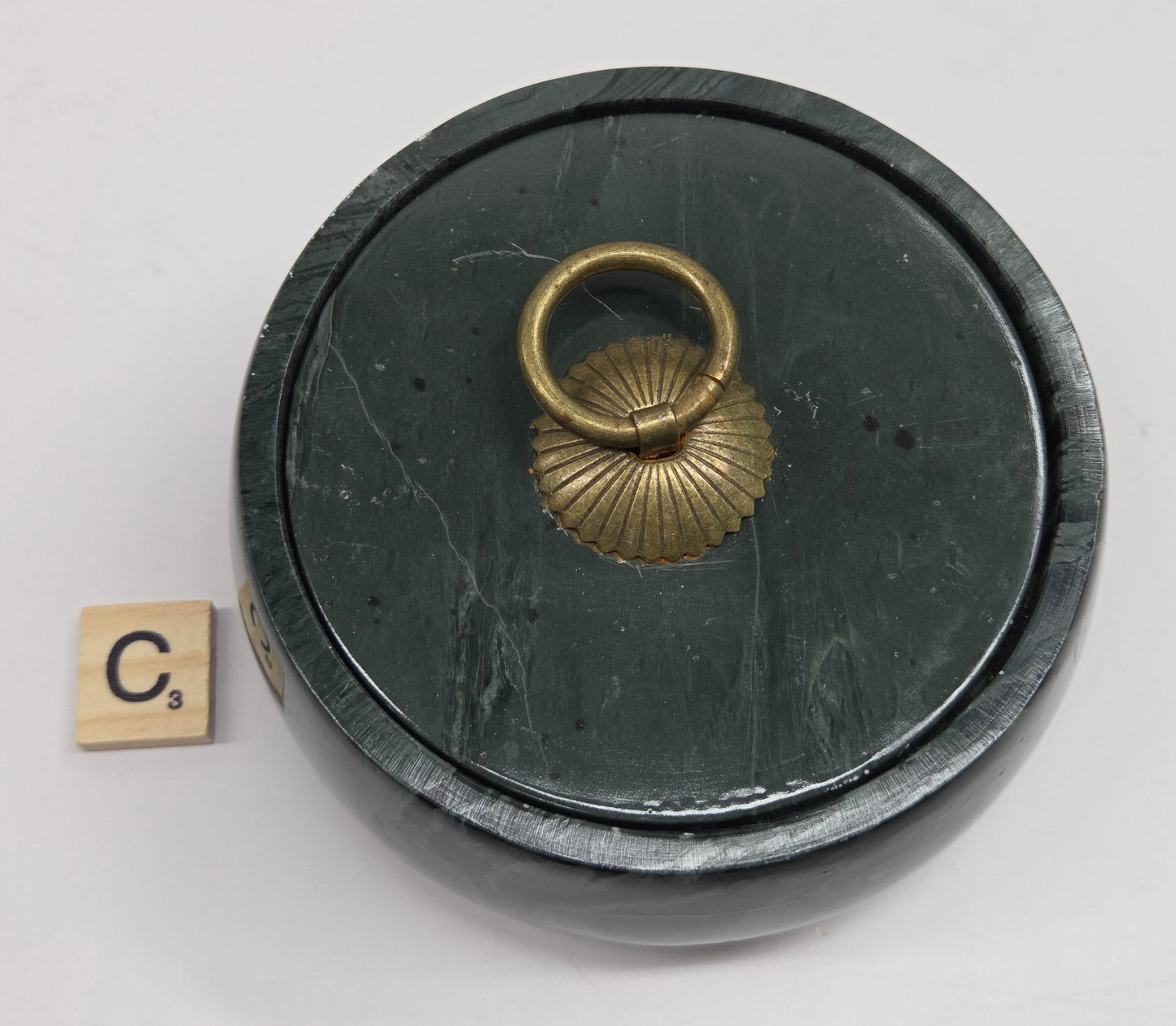 Round bowl container, with a gold colored handle on the lid, made of green wave picture jasper, with wave like patterns, on a white background