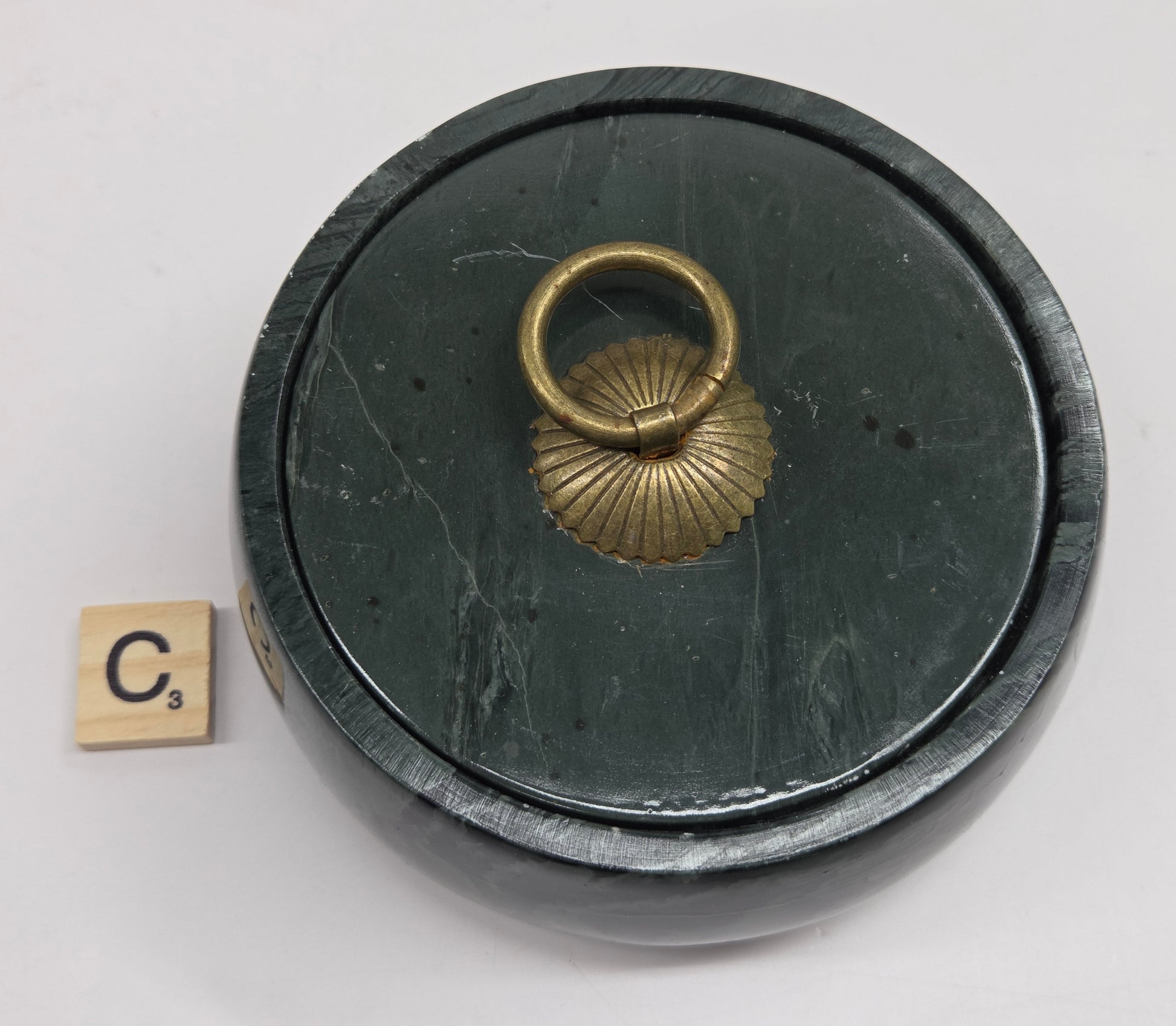 Round bowl container, with a gold colored handle on the lid, made of green wave picture jasper, with wave like patterns, on a white background