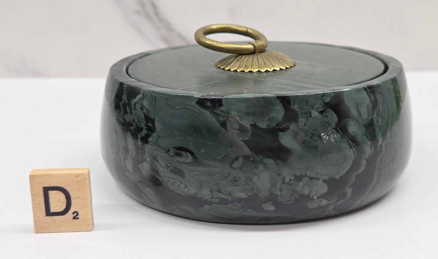 Round bowl container, with a gold colored handle on the lid, made of green wave picture jasper, with wave like patterns, on a white background