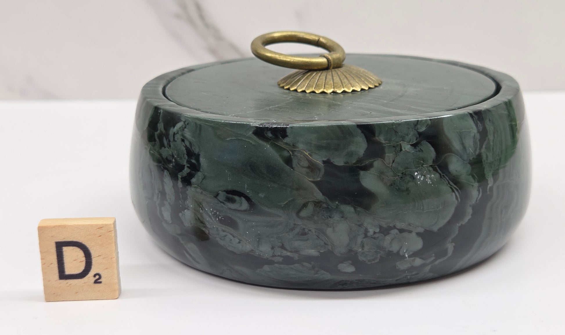 Round bowl container, with a gold colored handle on the lid, made of green wave picture jasper, with wave like patterns, on a white background