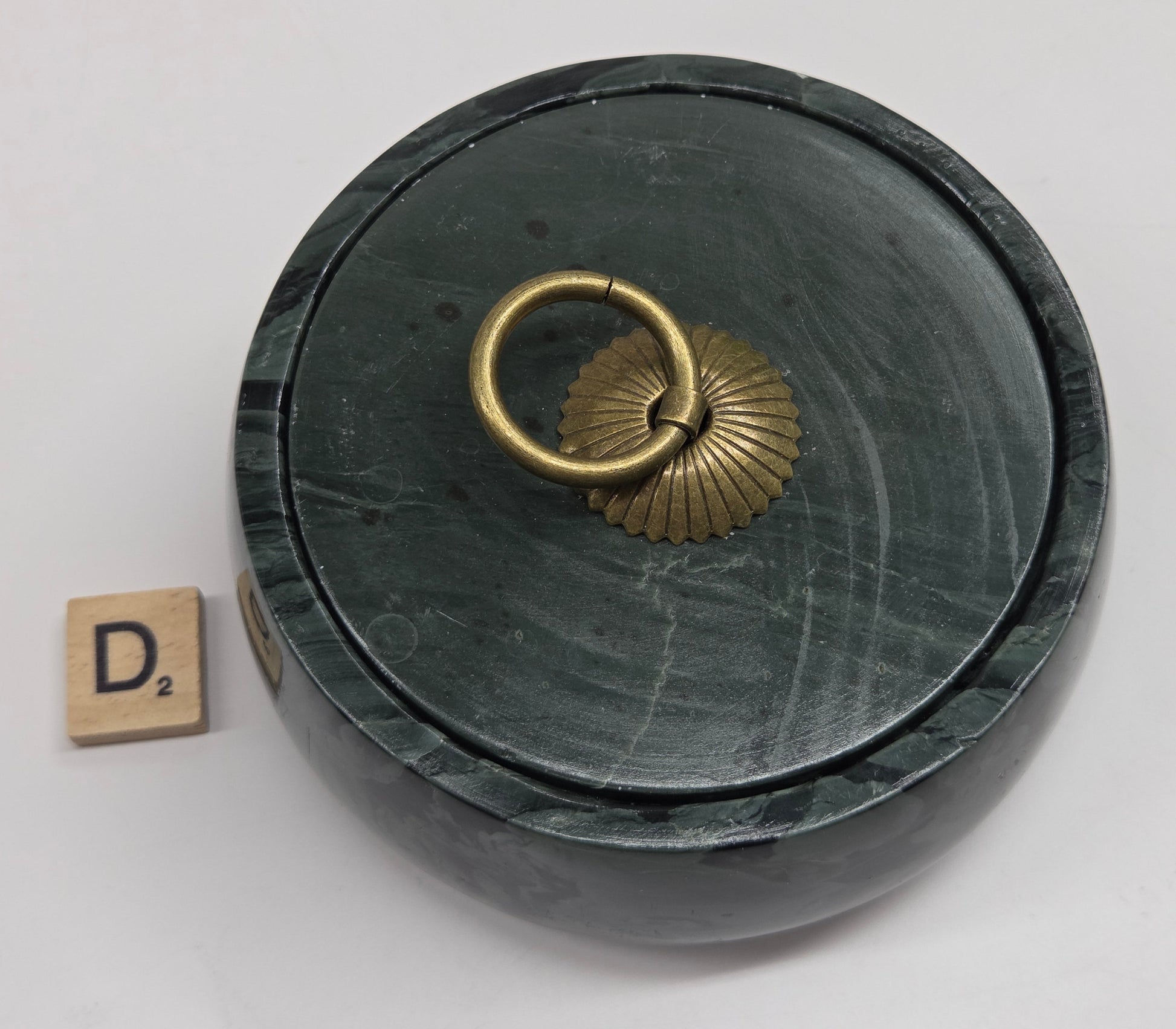 Round bowl container, with a gold colored handle on the lid, made of green wave picture jasper, with wave like patterns, on a white background