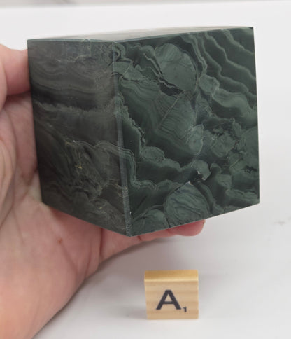 Hand holding a green wave picture jasper cube with a wave like pattern, on a white background