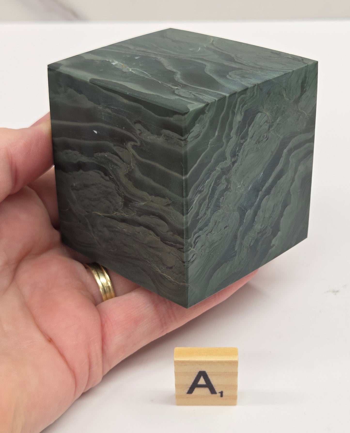 Hand holding a green wave picture jasper cube with a wave like pattern, on a white background