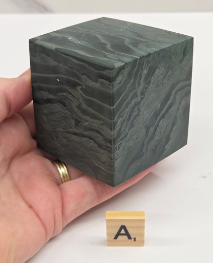 Hand holding a green wave picture jasper cube with a wave like pattern, on a white background