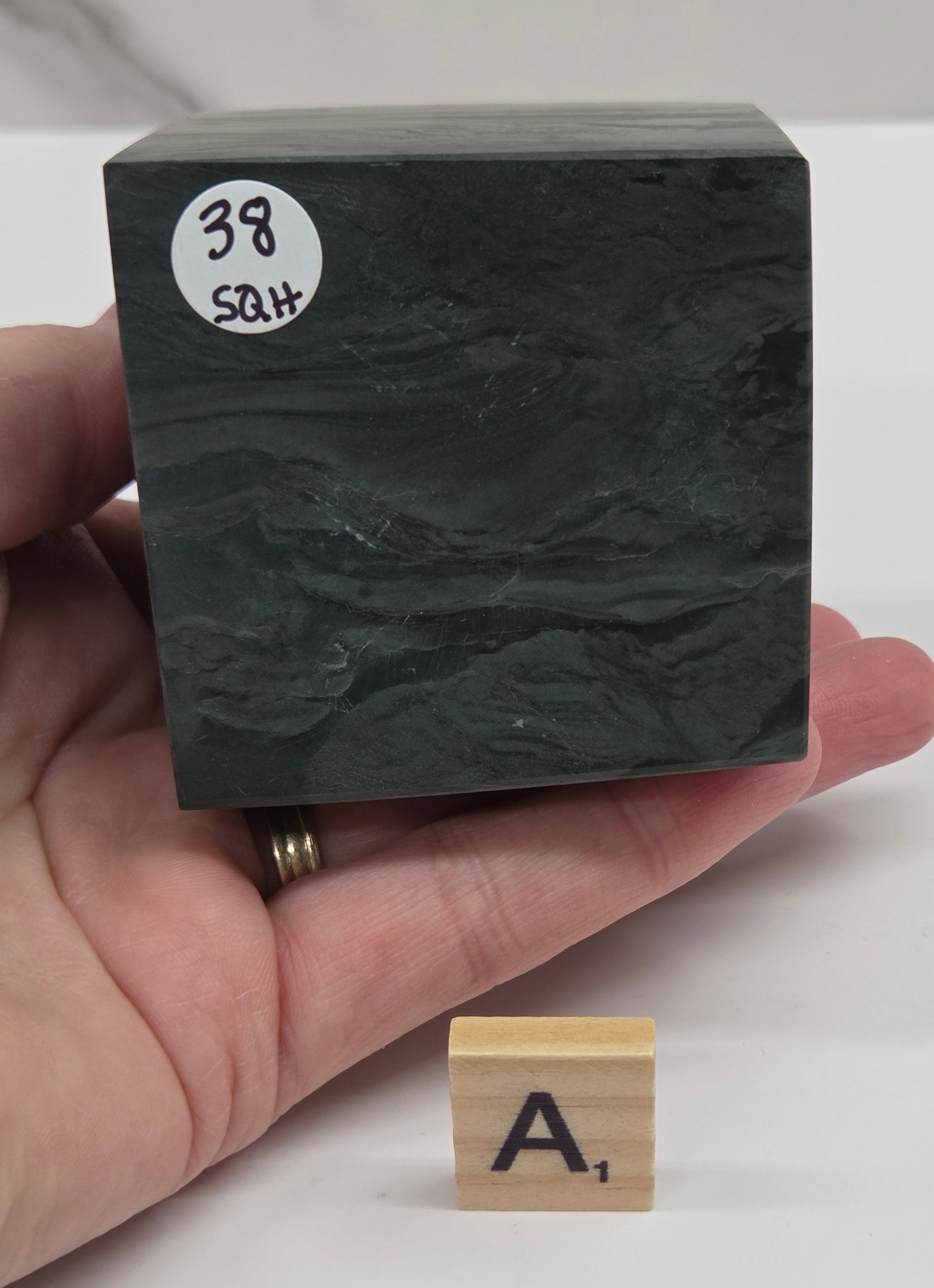 Hand holding a green wave picture jasper cube with a wave like pattern, on a white background