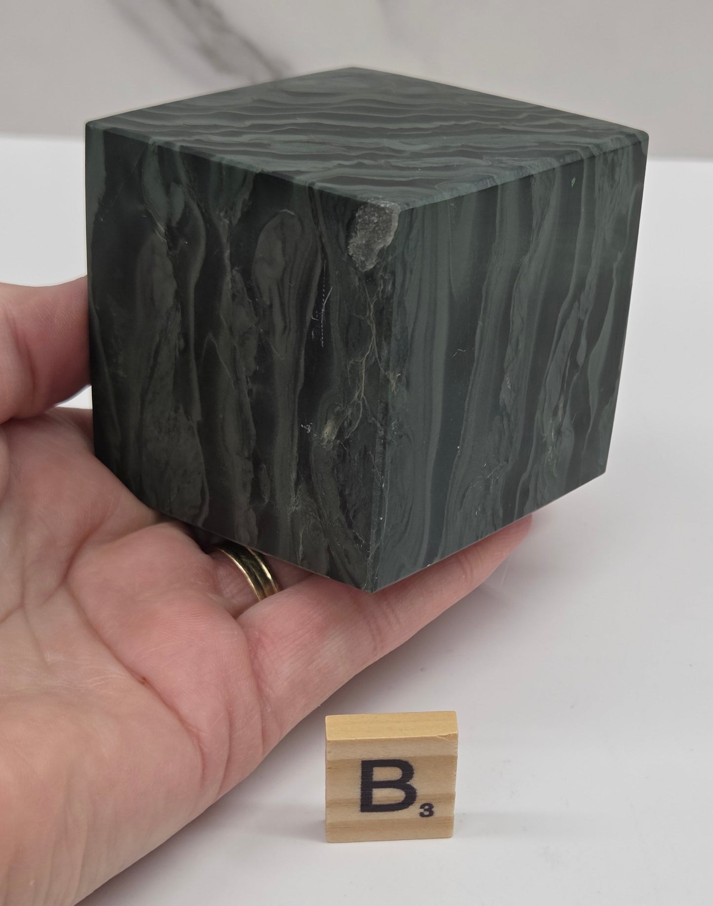 Hand holding a green wave picture jasper cube with a wave like pattern, on a white background