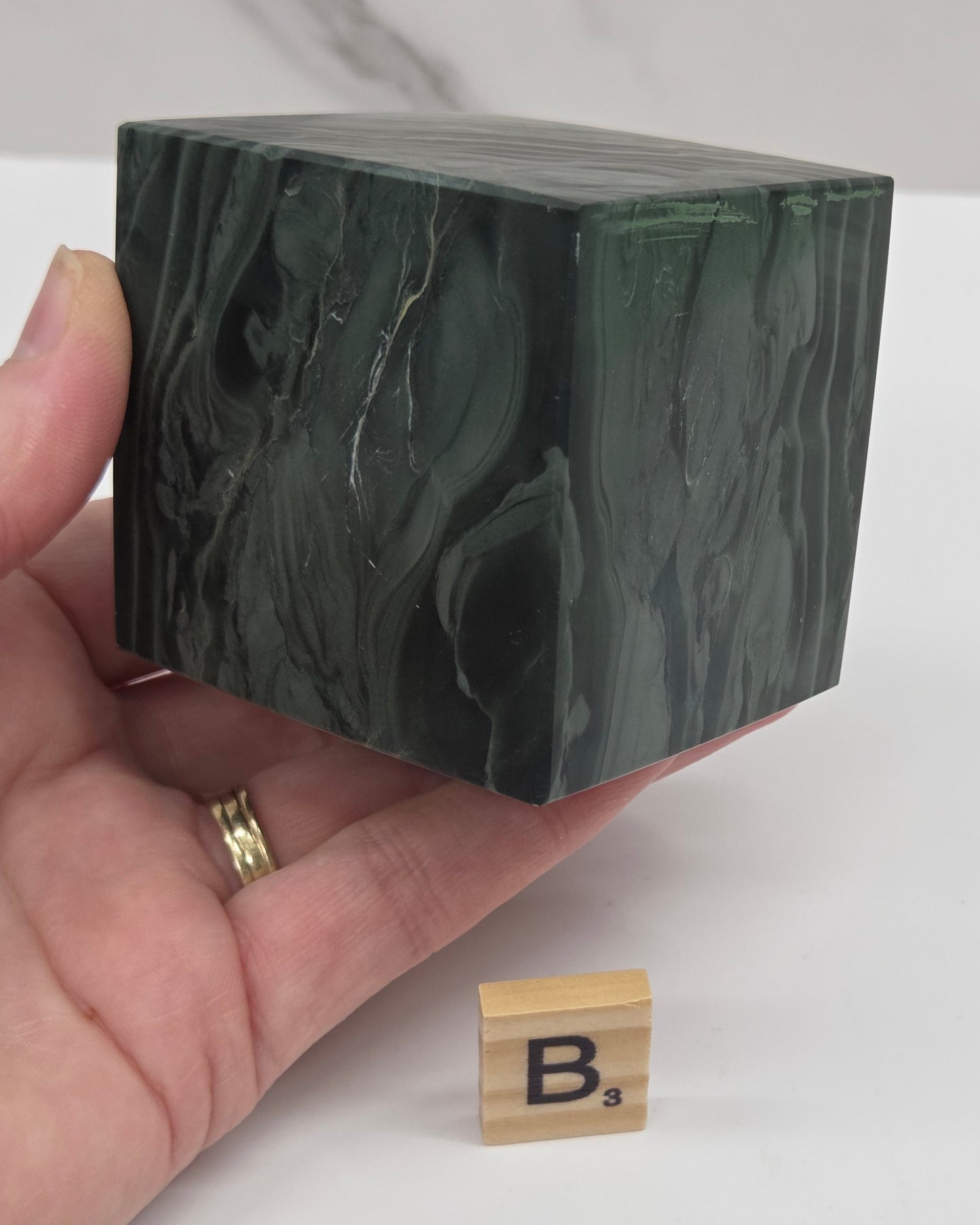 Hand holding a green wave picture jasper cube with a wave like pattern, on a white background