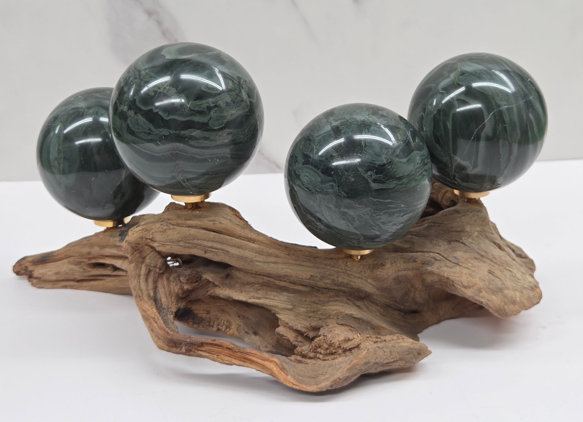 Set of green wave picture jasper spheres with a wave like pattern, on a driftwood stand, on a white background