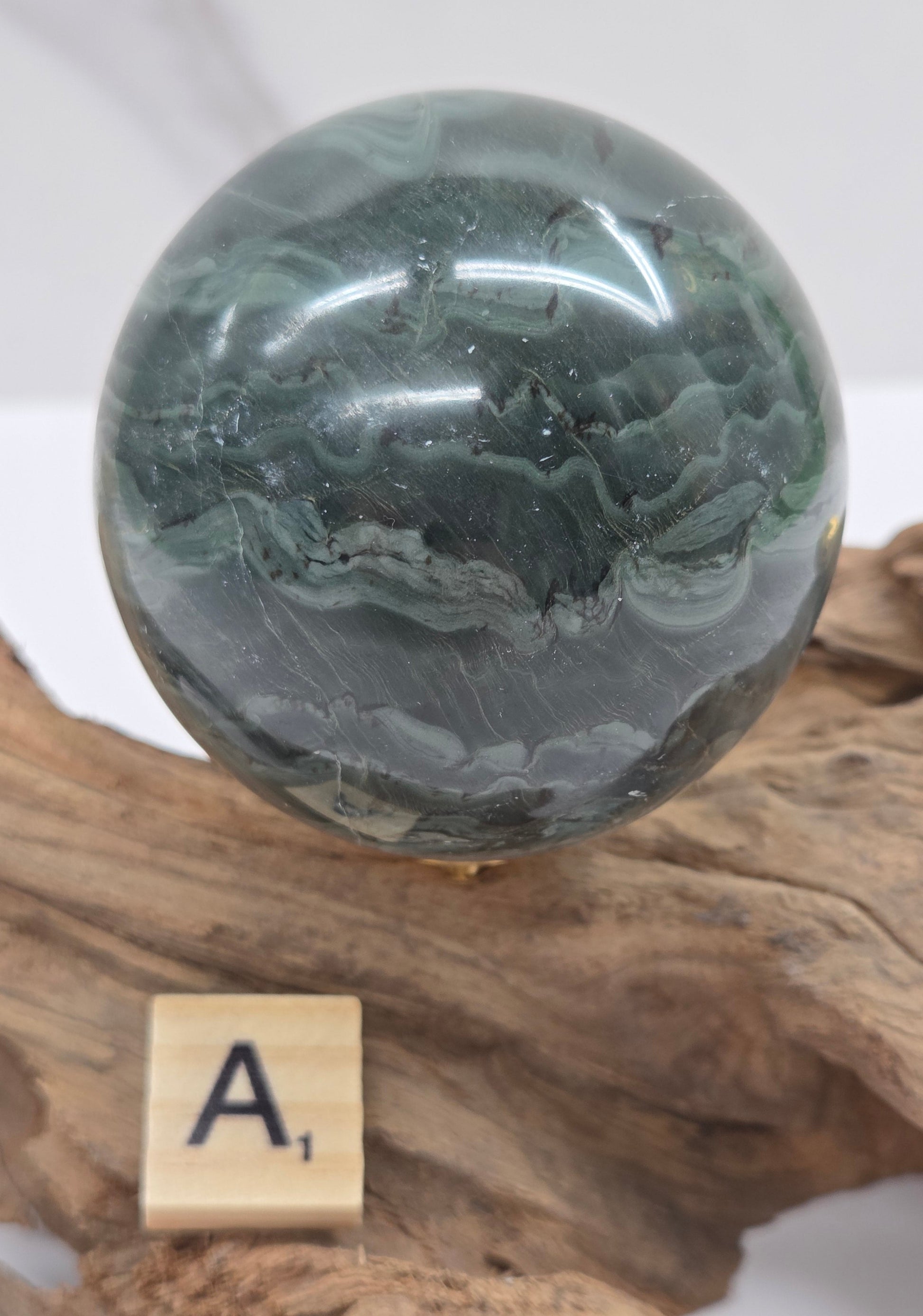 Green wave picture jasper sphere with a wave like pattern, on a driftwood stand, on a white background