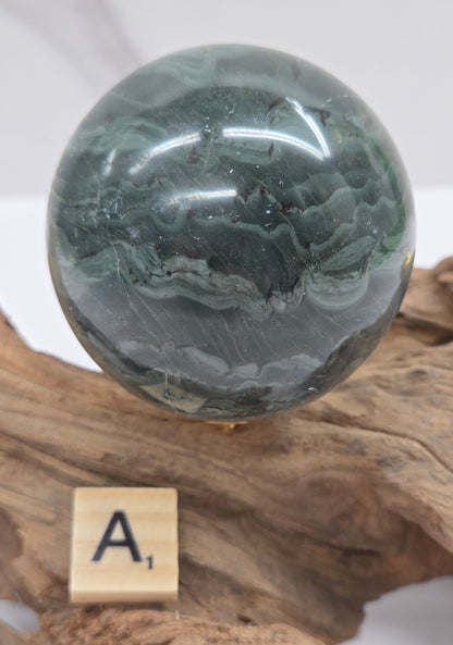 Green wave picture jasper sphere with a wave like pattern, on a driftwood stand, on a white background