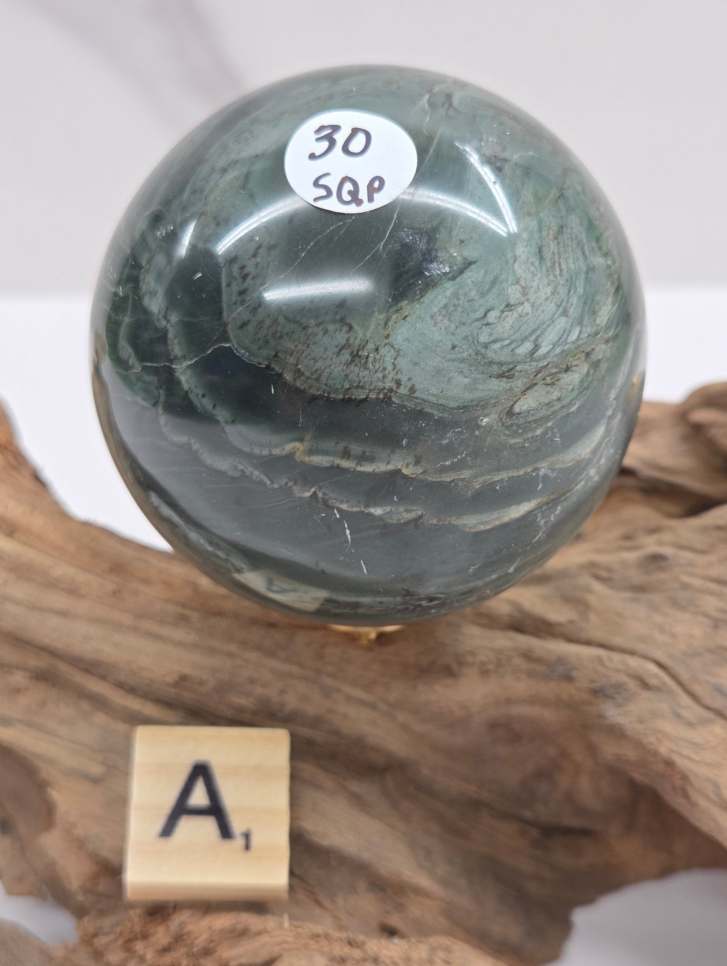Green wave picture jasper sphere with a wave like pattern, on a driftwood stand, on a white background