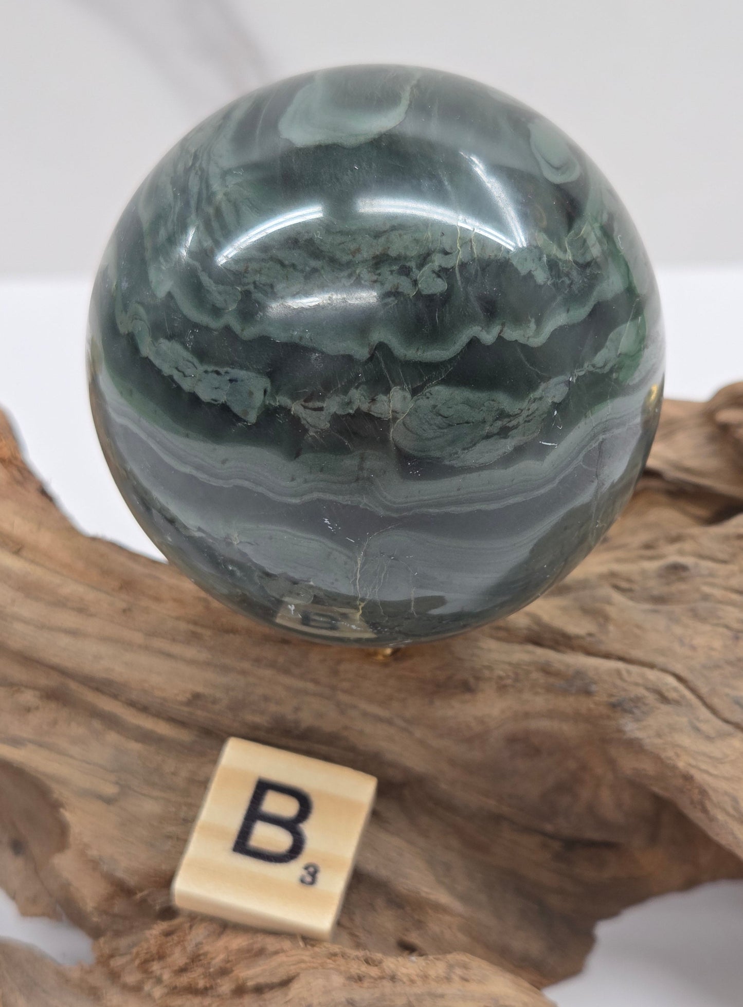 Green wave picture jasper sphere with a wave like pattern, on a driftwood stand, on a white background