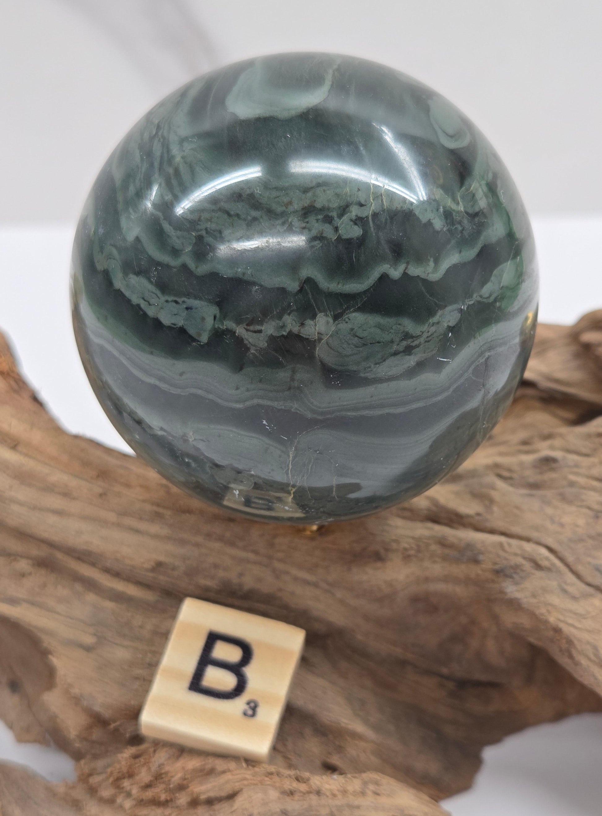 Green wave picture jasper sphere with a wave like pattern, on a driftwood stand, on a white background