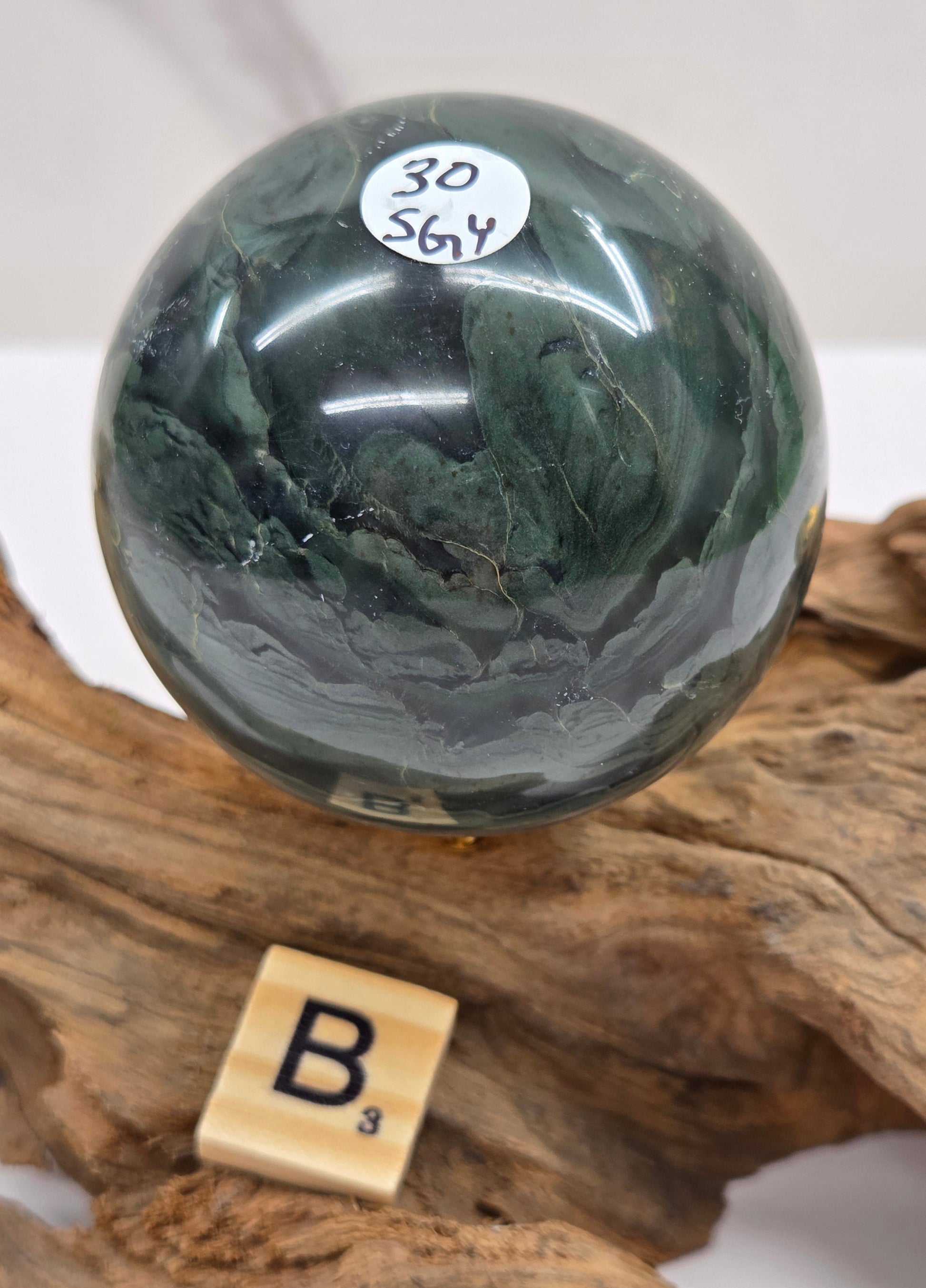 Green wave picture jasper sphere with a wave like pattern, on a driftwood stand, on a white background