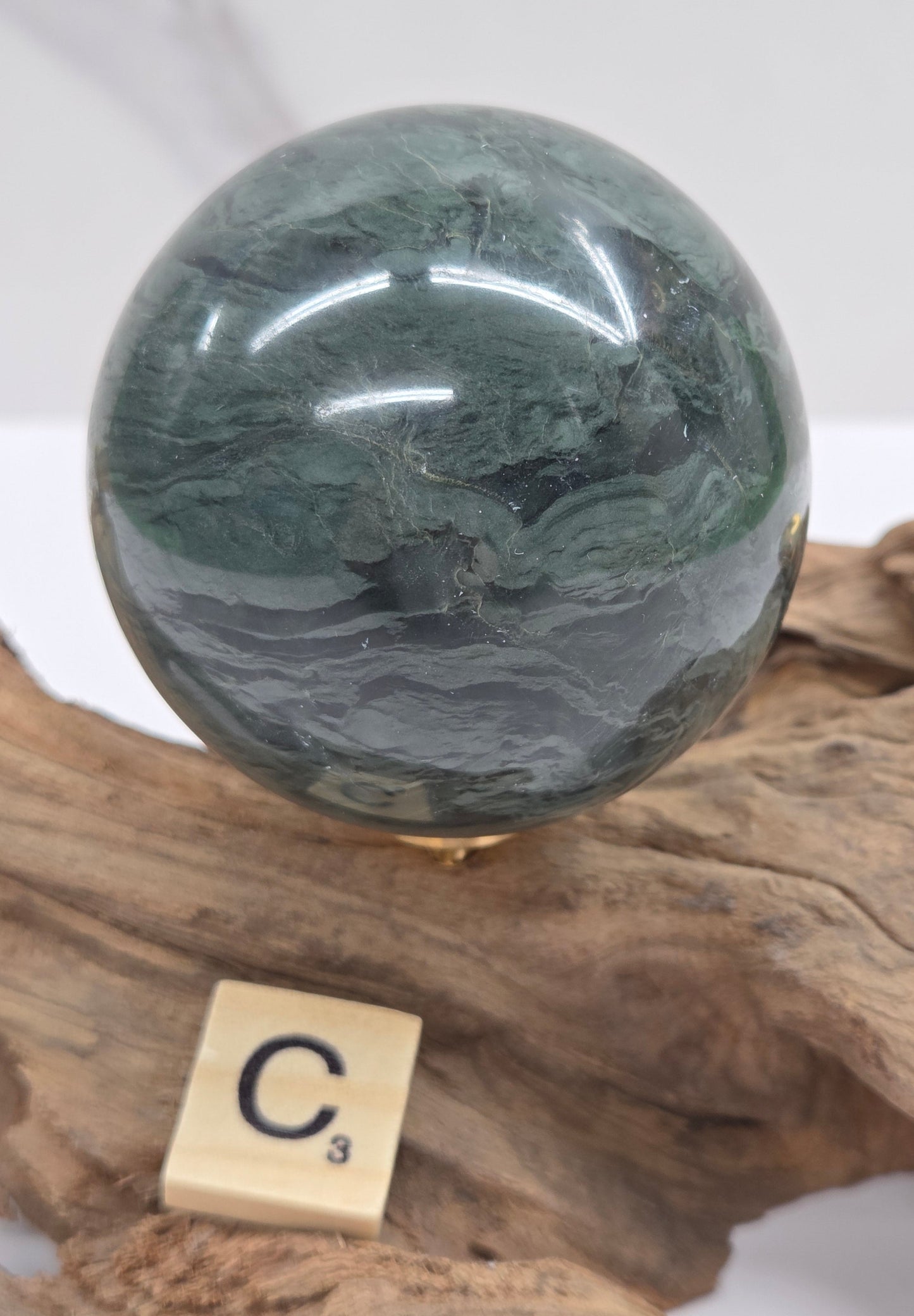Green wave picture jasper sphere with a wave like pattern, on a driftwood stand, on a white background