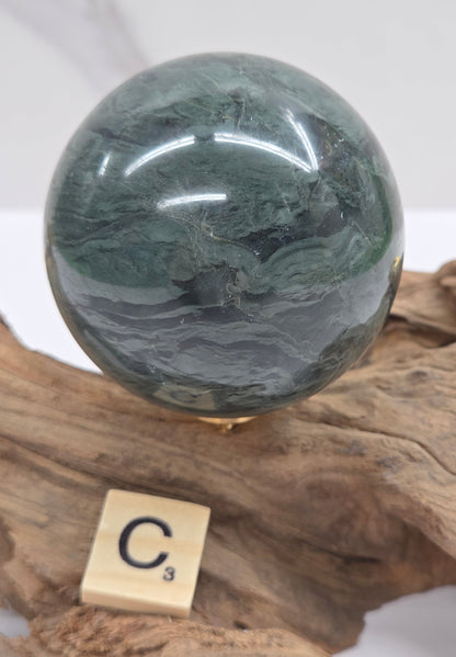 Green wave picture jasper sphere with a wave like pattern, on a driftwood stand, on a white background