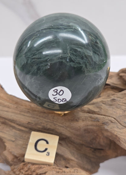 Green wave picture jasper sphere with a wave like pattern, on a driftwood stand, on a white background