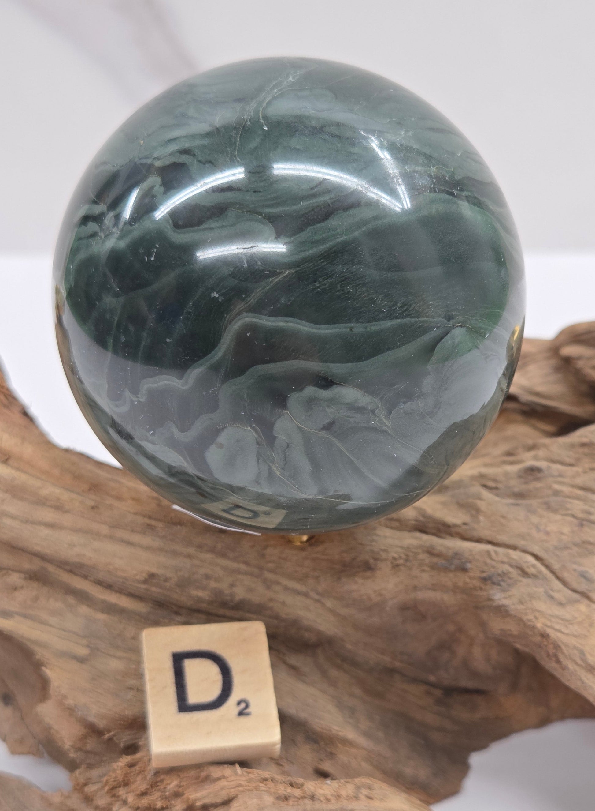Green wave picture jasper sphere with a wave like pattern, on a driftwood stand, on a white background