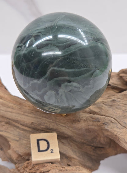 Green wave picture jasper sphere with a wave like pattern, on a driftwood stand, on a white background