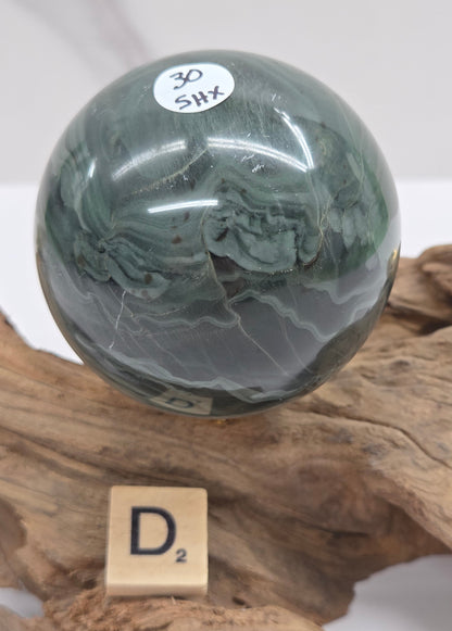 Green wave picture jasper sphere with a wave like pattern, on a driftwood stand, on a white background