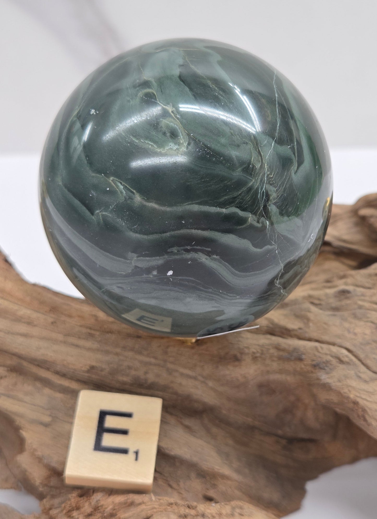 Green wave picture jasper sphere with a wave like pattern, on a driftwood stand, on a white background