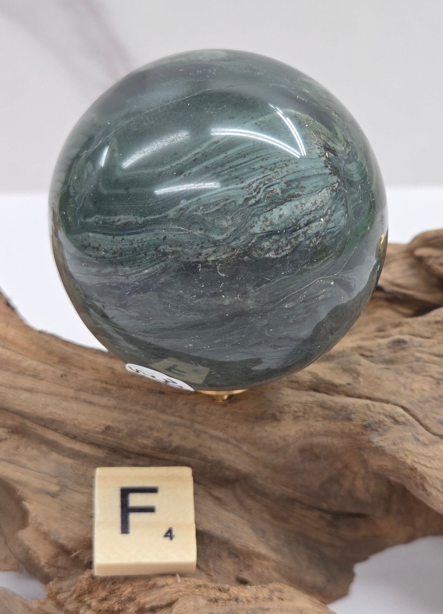 Green wave picture jasper sphere with a wave like pattern, on a driftwood stand, on a white background