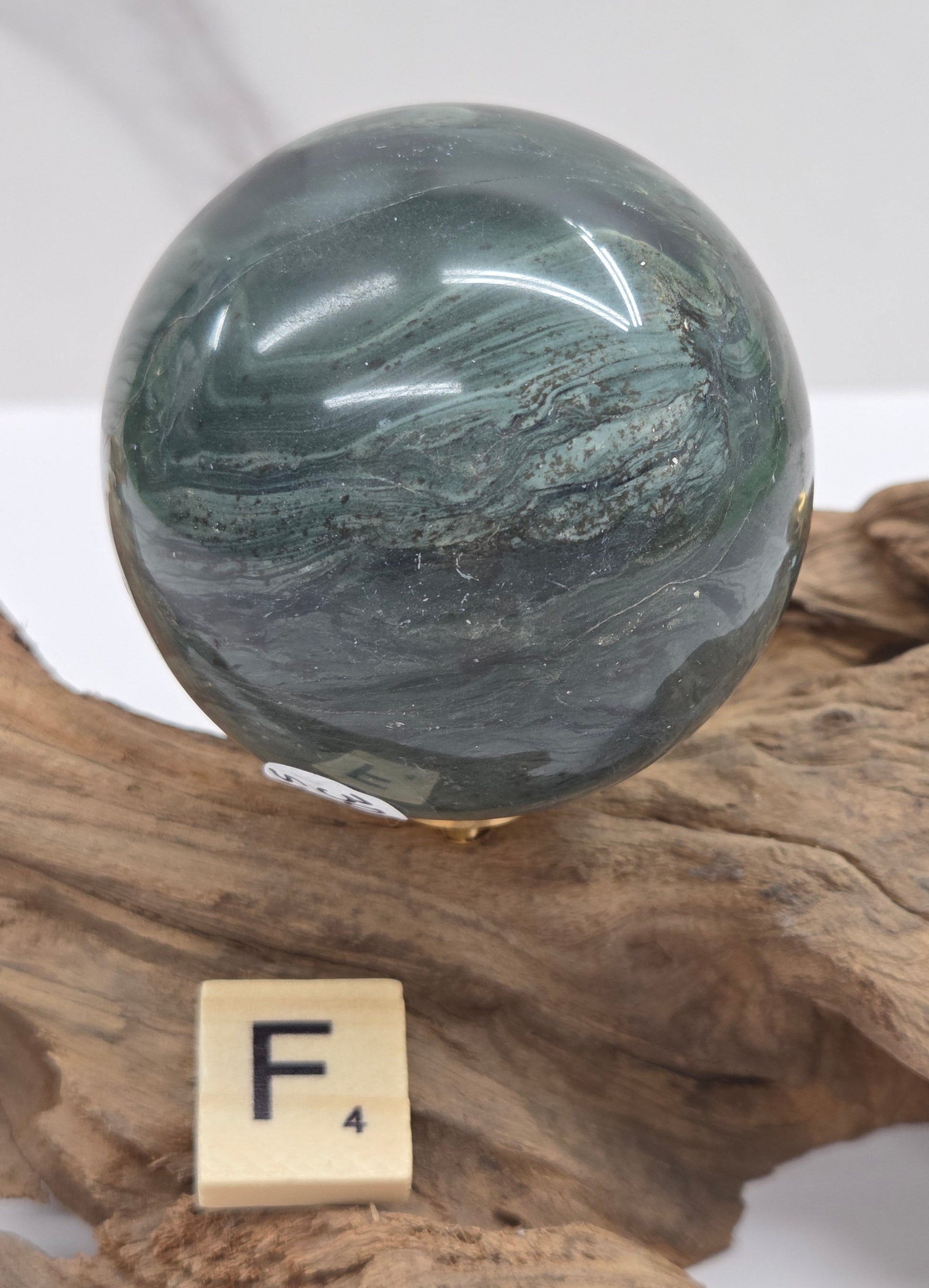 Green wave picture jasper sphere with a wave like pattern, on a driftwood stand, on a white background