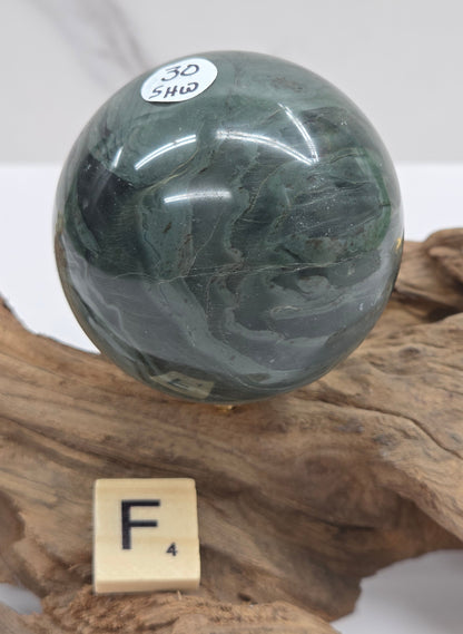 Green wave picture jasper sphere with a wave like pattern, on a driftwood stand, on a white background